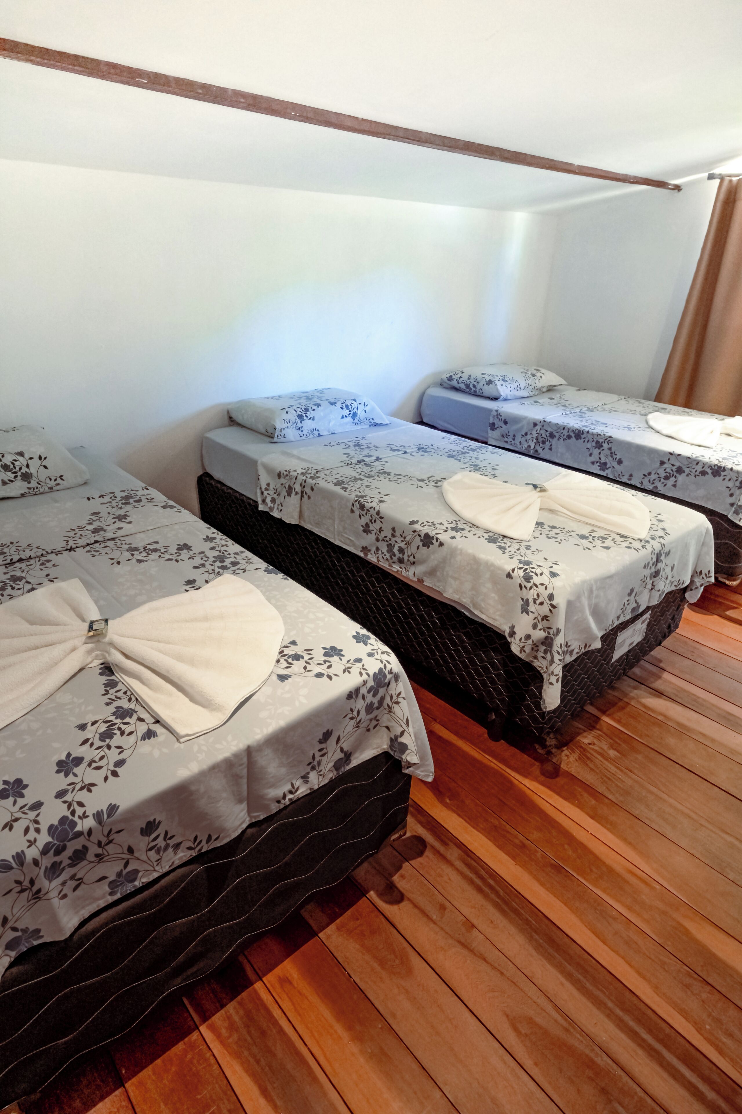 Une chambre avec trois lits, chacun recouvert d’une couvre-lit à motifs floraux et agrémenté d’un nœud décoratif. La chambre est dotée d’un plancher en bois et de murs blancs.