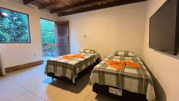 Quarto com duas camas, uma janela grande, teto de madeira e televisão na parede.