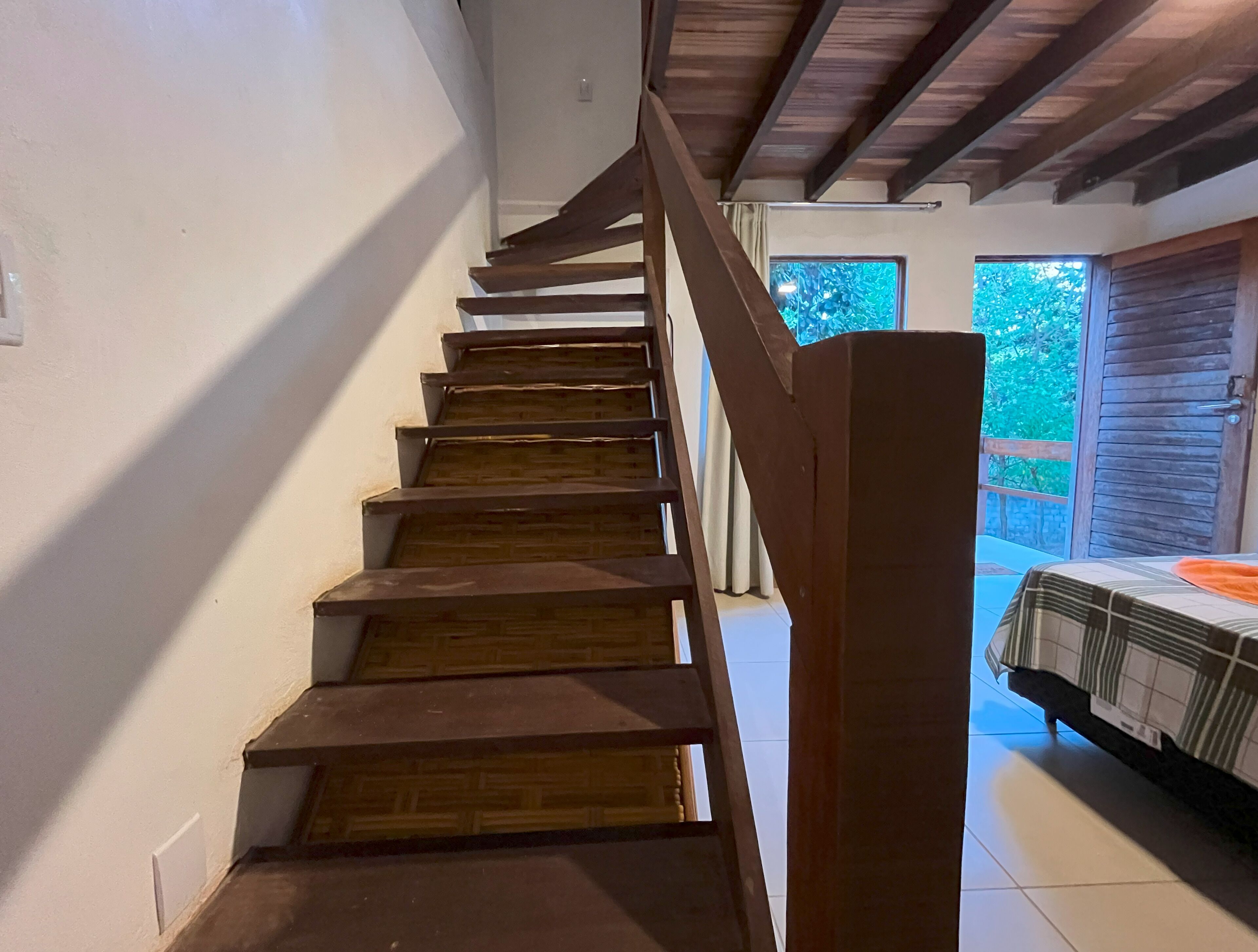 Una escalera de madera con barandilla que lleva a una habitación con cama y ventana.