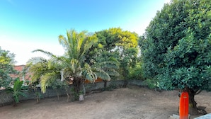 A backyard with a dirt ground, a brick wall, and various trees including a palm tree. - Pousada em Lençóis Reserva do Dendê (Lençóis)