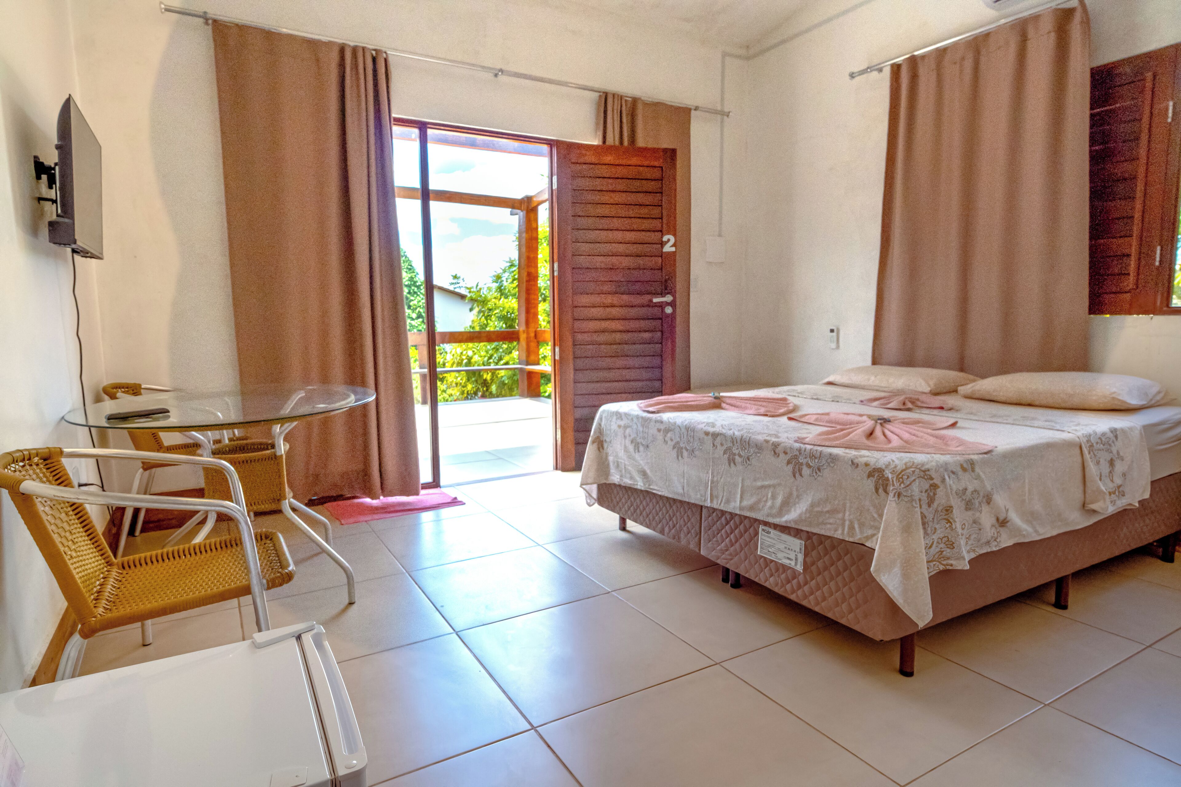 A bedroom with a bed, a chair, a table, and a sliding glass door leading to a balcony.