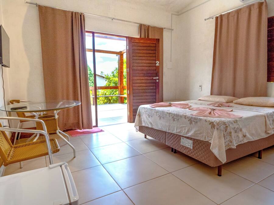 A bedroom with a bed, a chair, a table, and a sliding glass door leading to a balcony.