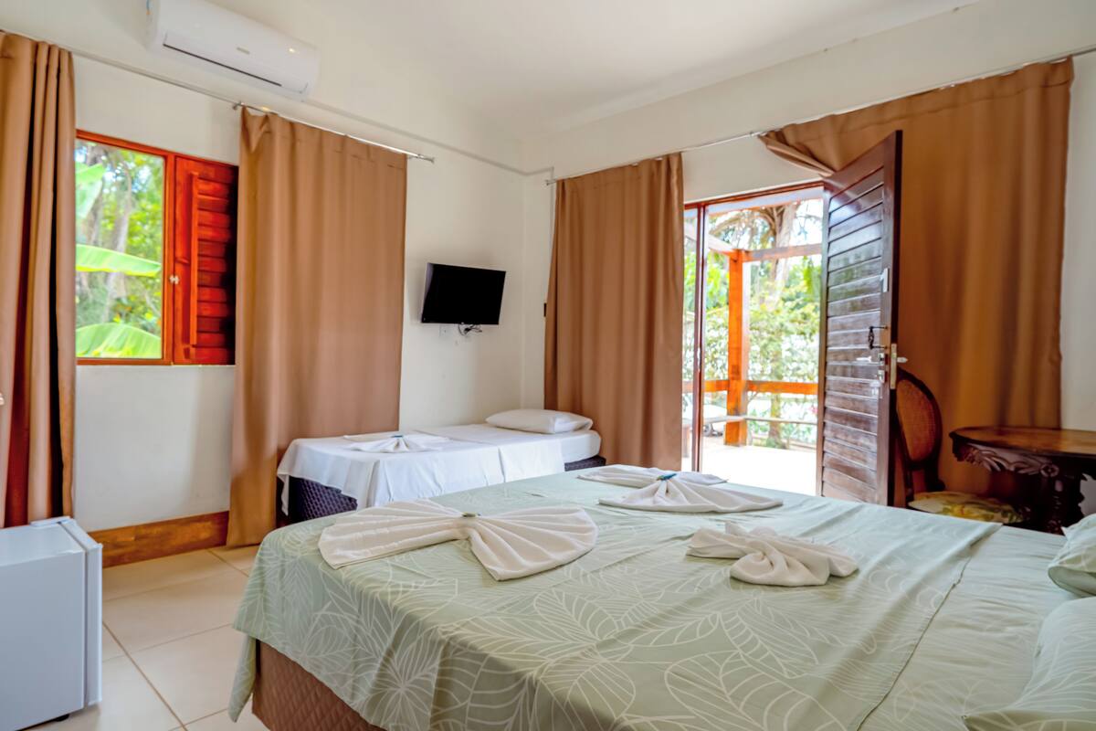 A hotel room with a bed, a desk, a chair, a TV, and a sliding door to an outdoor area.
