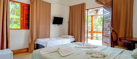 A hotel room with a bed, a desk, a chair, a TV, and a sliding door to an outdoor area.