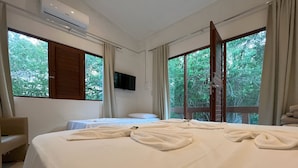 A hotel room with a large bed, two smaller beds, a TV, and a view of trees through the windows. - Pousada em Lençóis Reserva do Dendê (Lençóis)