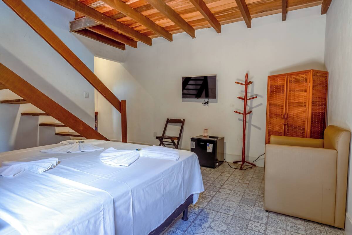 A bedroom with a bed, a small table, a chair, a TV, and a wardrobe.