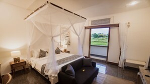 A bedroom with a bed, a black sofa, a nightstand, a lamp, and a view of the outdoors. - Daysha Ubud (Ubud)