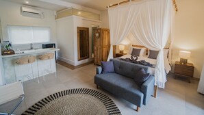 A bedroom with a bed, a sofa, a bedside table, a nightstand, a lamp, a mirror, a wardrobe, a desk with chairs, and a small kitchen area. - Daysha Ubud (Ubud)