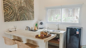 A small kitchen with a bar area, a refrigerator, and a window with a view of greenery. - Daysha Ubud (Ubud)