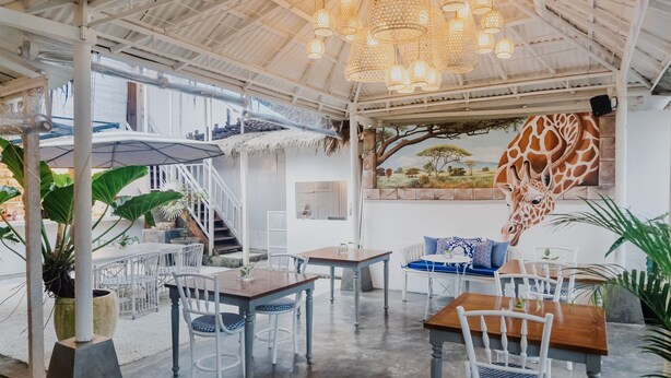 An indoor dining area with white and wooden tables and chairs, a staircase, and a giraffe mural on the wall. - Daysha Ubud (Ubud)