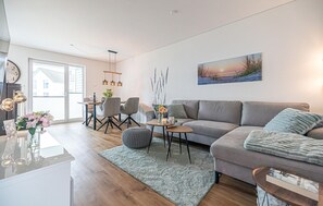 Uma sala de estar moderna com um sofá cinzento, uma mesa de centro e uma área de jantar com cadeiras e uma mesa.