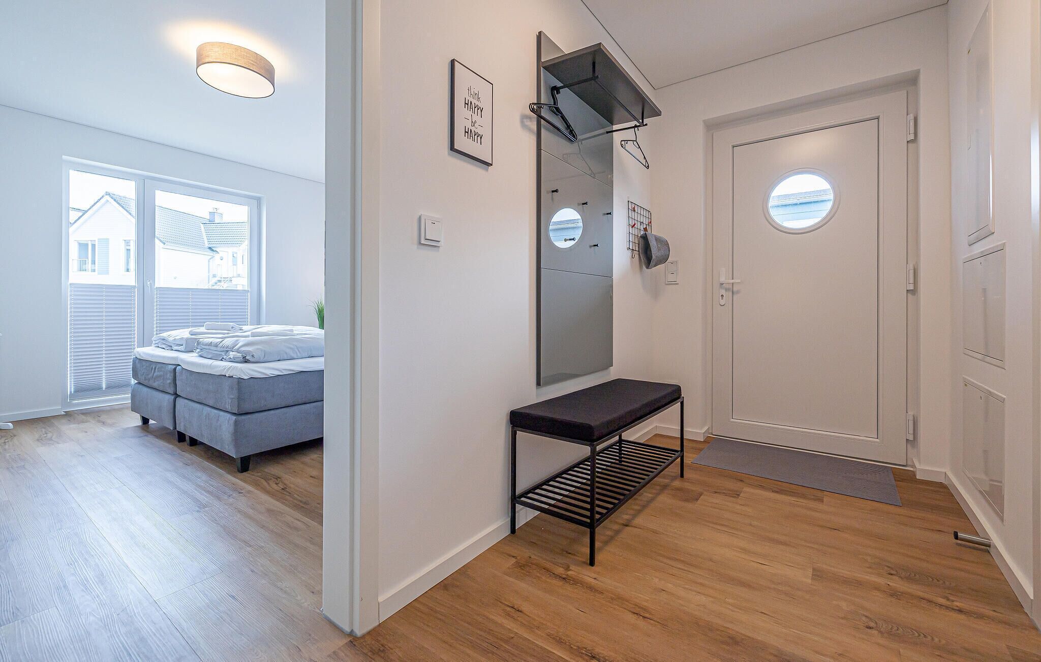 Un intérieur moderne avec un canapé gris, un banc, un miroir et une porte dotée d’une fenêtre circulaire.