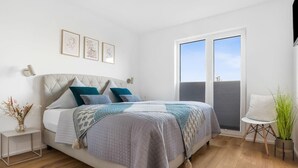 A bedroom with a bed, a bedside table, a chair, a window, and a wall-mounted TV.