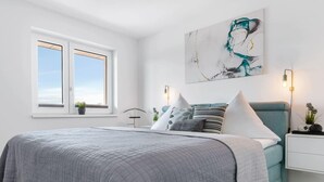 A modern bedroom with a large bed, a window with a view, a wall-mounted abstract painting, and bedside lamps. - Stunning apartment in Olpenitz (Olpenitz)