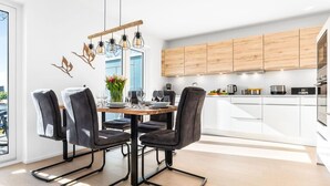 A modern dining area with a wooden table and black chairs, a chandelier, and a vase of flowers.