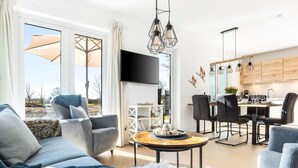 A spacious living area with a sofa, a coffee table, and a TV. There is a dining area with chairs and a table.