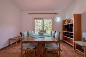 A dining area with a wooden table, chairs, a bench, a window with a view, and a wooden shelf unit.