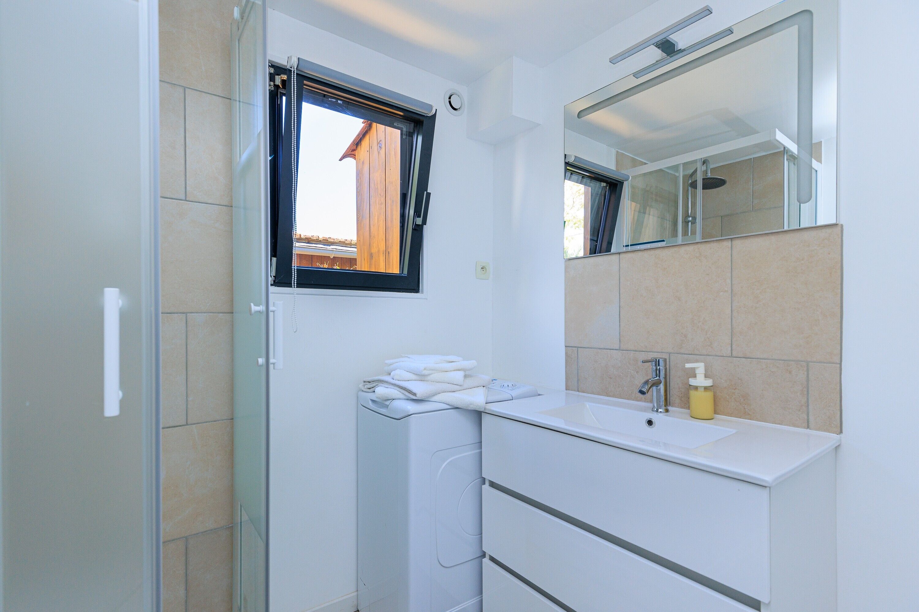 Une salle de bain moderne équipée d’un lave-linge intégré, d’un lavabo avec miroir et d’une fenêtre.