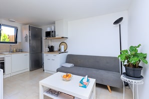 Um espaço compacto com cozinha compacta, sofá, mesa de centro com frutas e uma planta em vaso.