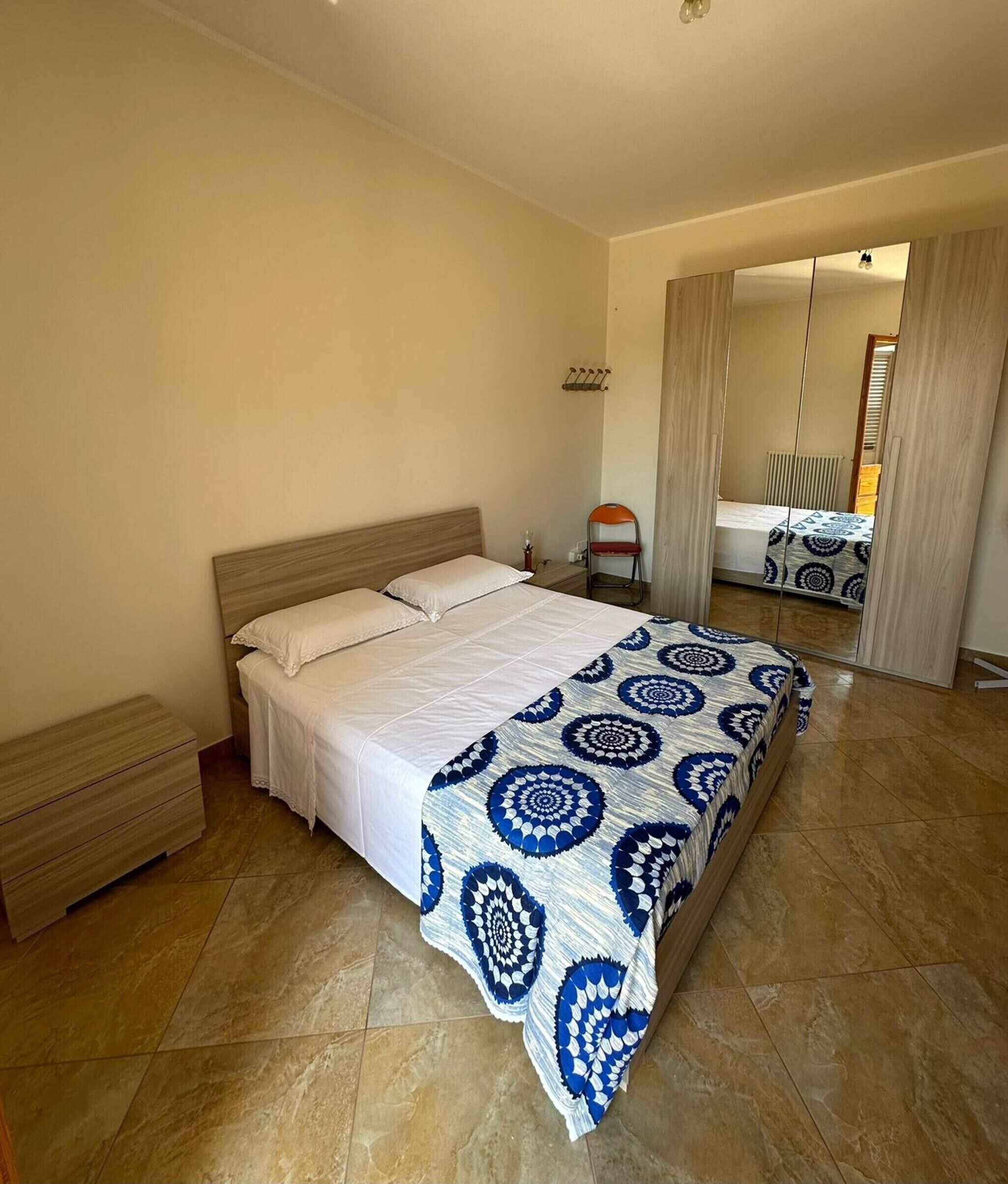 Ein Schlafzimmer mit einem großen Bett, einem Nachttisch, einem Stuhl, einem Kleiderschrank und einem Spiegel.