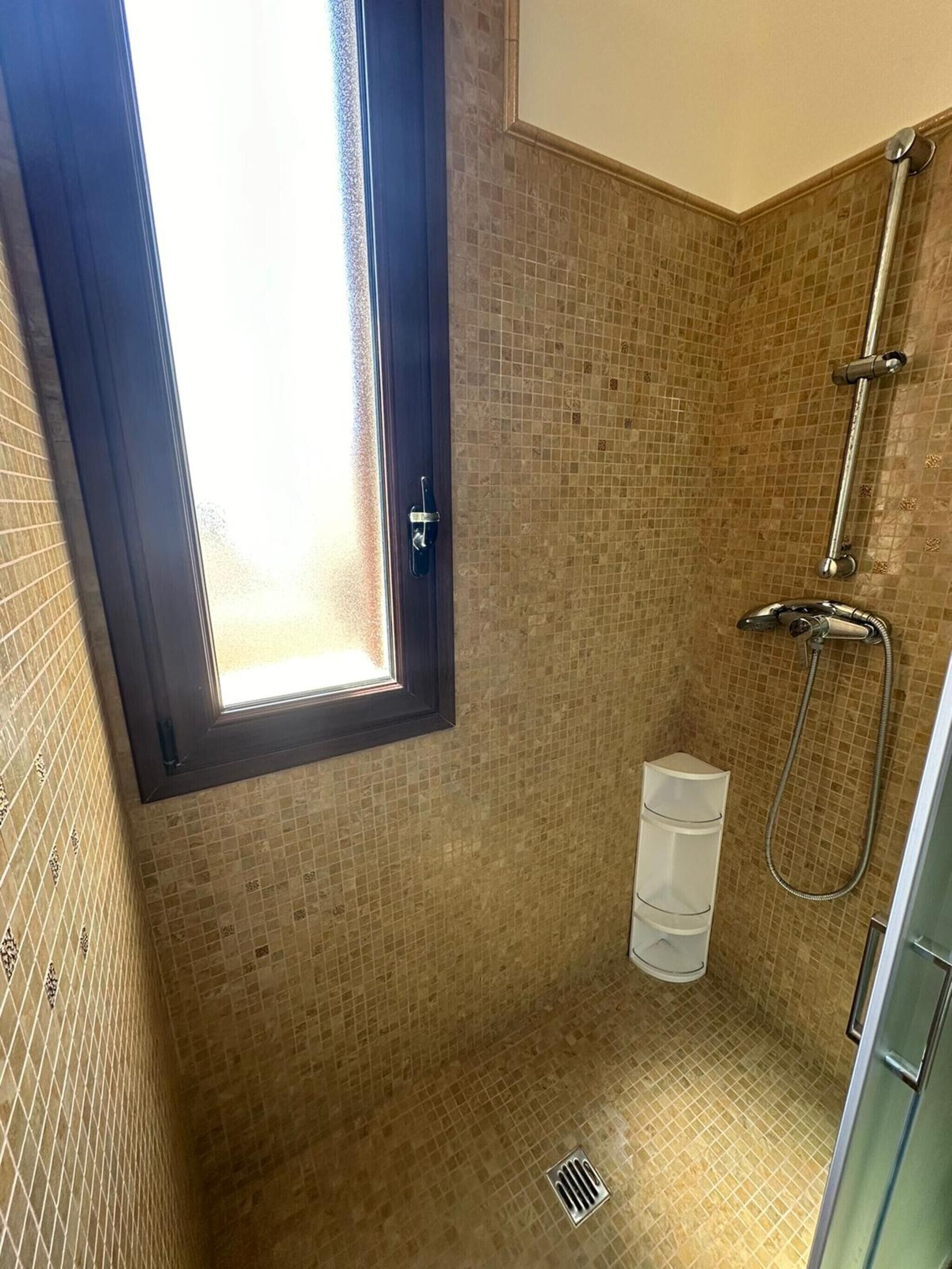 Une douche avec une fenêtre, des murs carrelés et un pommeau de douche en métal.