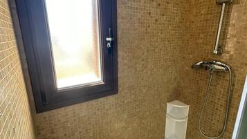 Une douche avec une fenêtre, des murs carrelés et un pommeau de douche en métal.