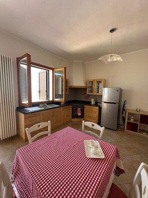 A compact kitchen with wooden cabinets, a stainless steel refrigerator, a dining table with a checkered tablecloth, and a window with blinds. - Holiday Home 'Da Katia' with Private Terrace, Balcony and Air Conditioning (Arnesano)