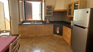 A kitchen with a stove, refrigerator, wooden cabinets, and a dining table with a red and white checkered tablecloth. - Holiday Home 'Da Katia' with Private Terrace, Balcony and Air Conditioning (Arnesano)