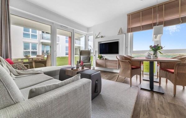 A modern living room with a sofa, dining table, and chairs. There is a TV mounted on the wall and a window with a view of the sea. - Gorgeous apartment in Olpenitz with sauna (Olpenitz)