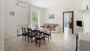 A dining area with a table and chairs, a sofa, and a television on a stand. - Villa 'Azzurra' with Sea View, Wi-Fi and Air Conditioning (Massa Lubrense)