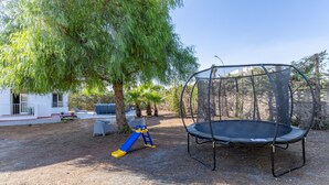 Patio trasero con un trampolín, un tobogán y un árbol.