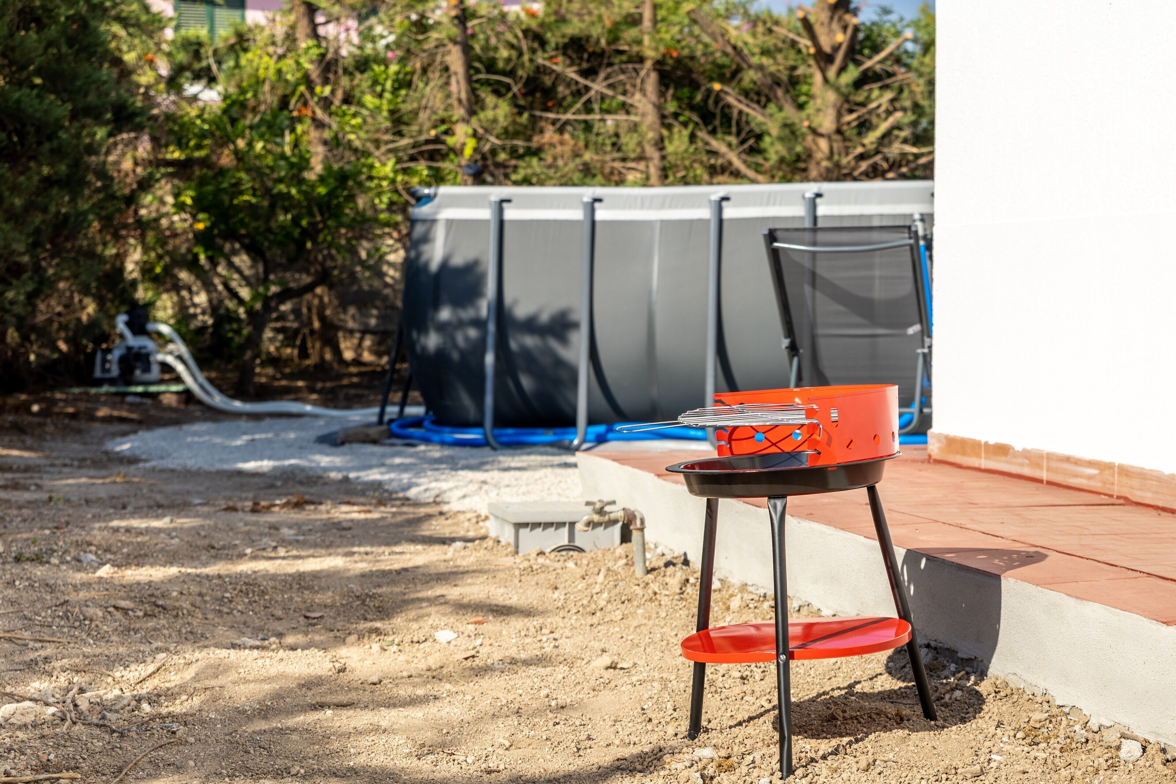 Eine Terrasse mit einem roten Stuhl, einem kleinen Tisch und einem blauen Gartenschlauch.