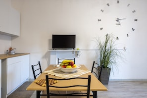 A dining area with a table, chairs, a bowl of fruit, a clock, and a television.