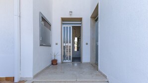 Uma entrada limpa e moderna, com planta em vaso, porta com painéis de vidro e luminária acima.