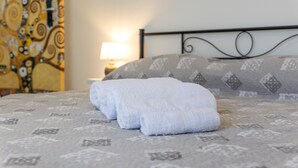 Cama bem arrumada com toalhas dobradas, colcha estampada e um detalhe decorativo na parede.