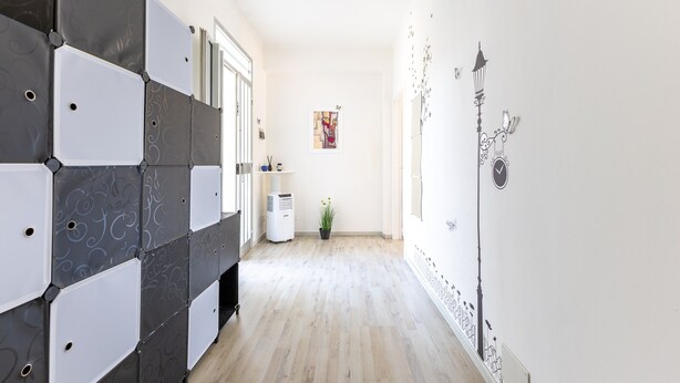 Um corredor com design moderno, apresentando um móvel geométrico na parede, uma planta em vaso e um aplique.