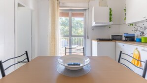 Uma sala de jantar com uma mesa, cadeiras, uma tigela e uma cozinha ao fundo.