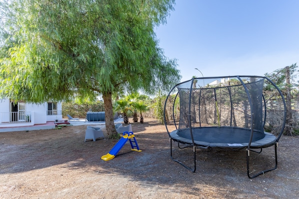 Ein Garten mit Trampolin, Rutsche und Baum.