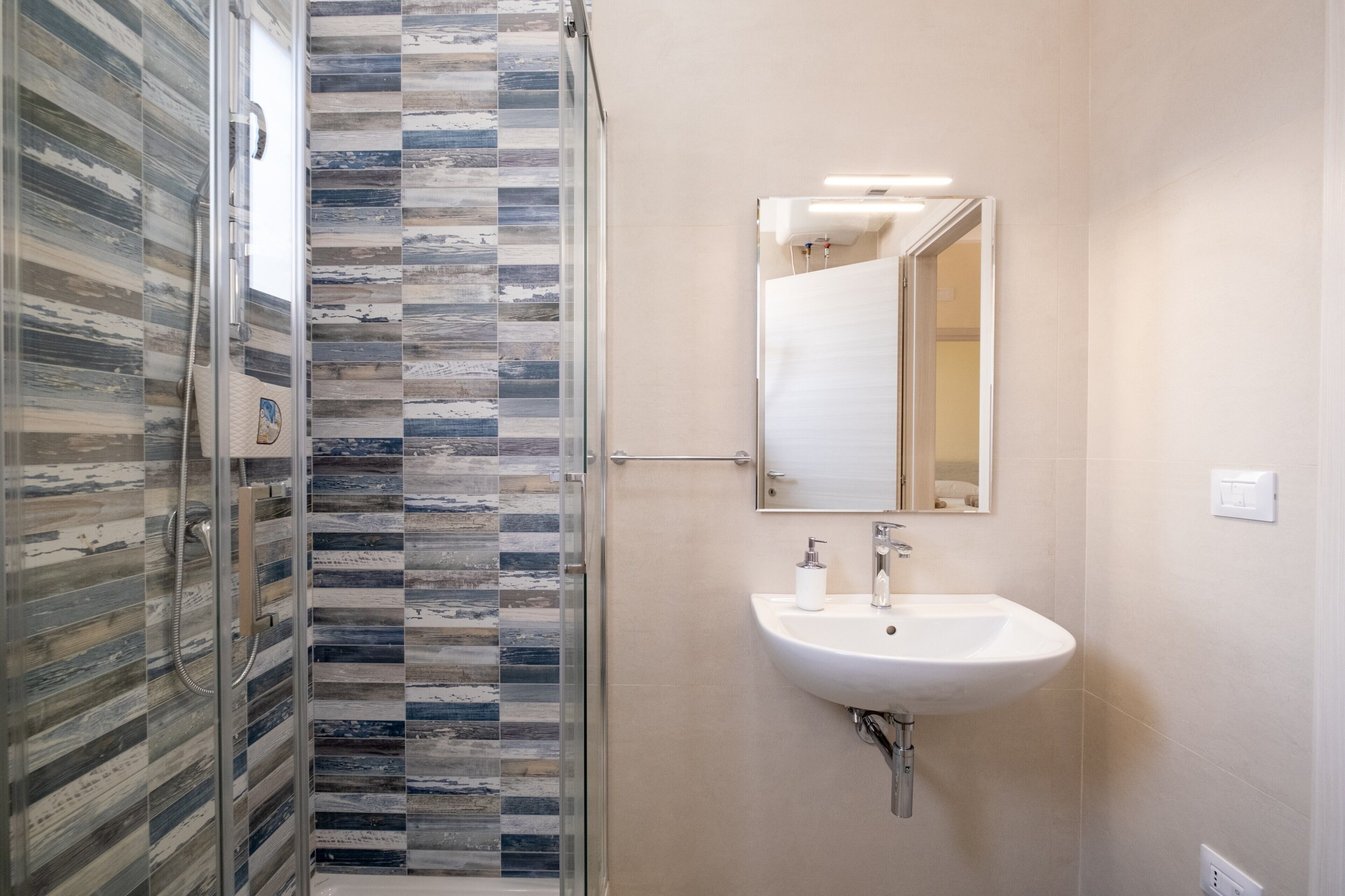 Ein Badezimmer mit Duschkabine aus Glas, Waschbecken mit Spiegel und Fliesenwand.