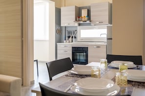 Une cuisine moderne avec des meubles blancs, un four encastré et une table à manger pour quatre personnes.