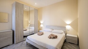 Een moderne slaapkamer met een grote spiegel, een bed met netjes opgevouwen handdoeken, nachtkastjes en een kledingkast.