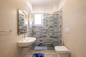 A bathroom with a sink, toilet, shower, and a window.