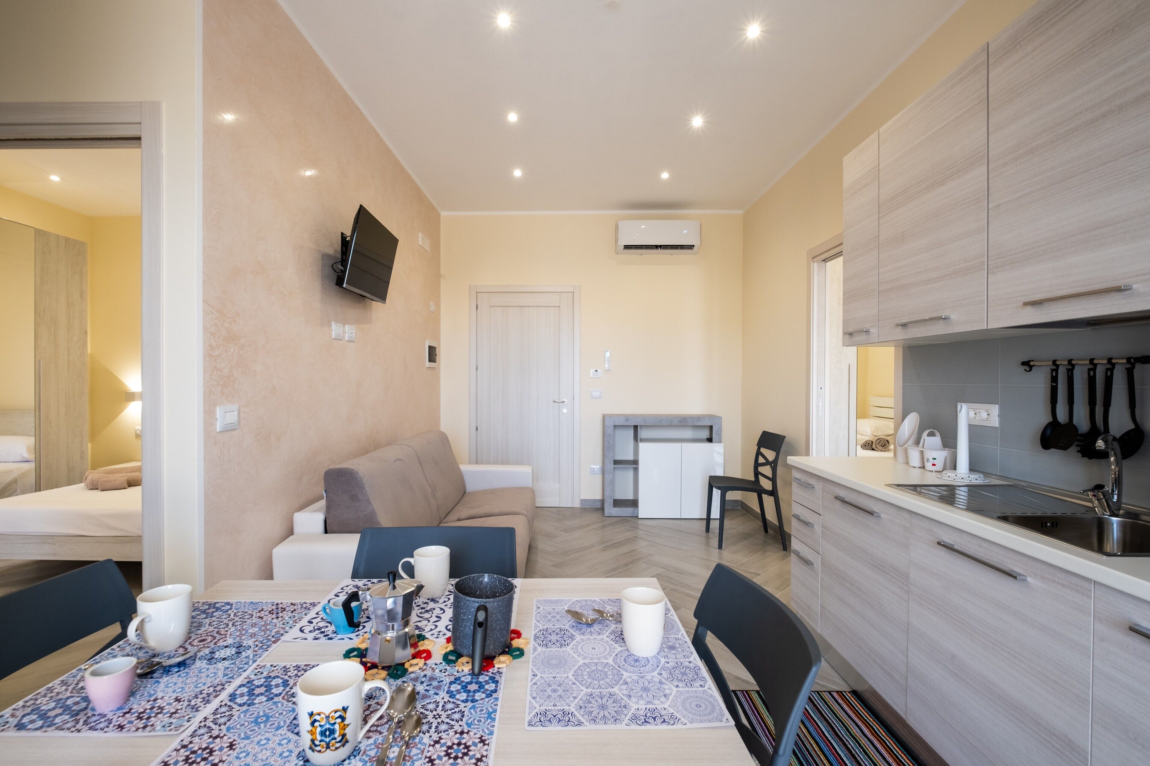 Habitación de hotel compacta con comedor, kitchenette y televisor montado en la pared.