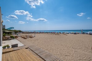 A beach with a wooden deck, umbrellas, and beach chairs.