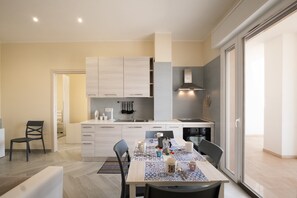 A modern kitchen with white cabinets, a dining table with chairs, and a view through a glass door.