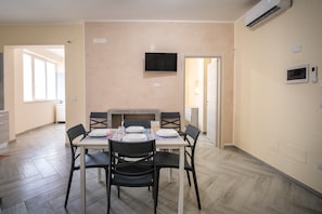 A dining area with a table set for four, a flat-screen TV mounted on the wall, and an air conditioning unit. - Apartment 'i Portici Unità 104' with Wi-Fi (san pietro in bevagna)