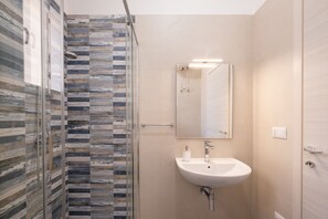 A bathroom with a glass shower enclosure, a sink, and a mirror.