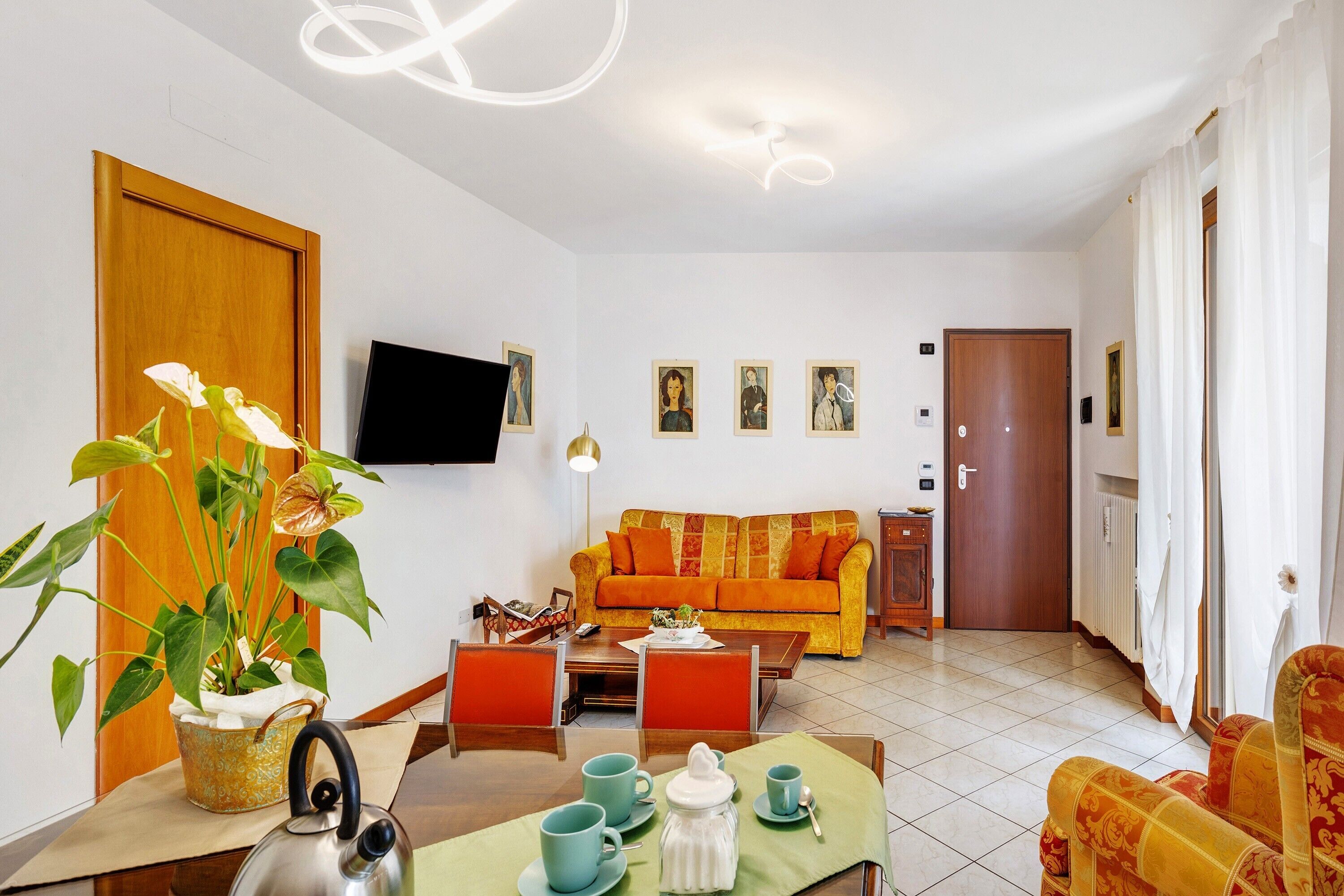 Una sala de estar con sofá, una mesa de comedor con sillas, televisión y una planta en maceta.