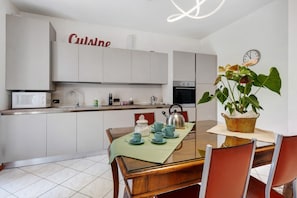 A modern kitchen with white cabinets, a microwave, a kettle, and a dining table with chairs.