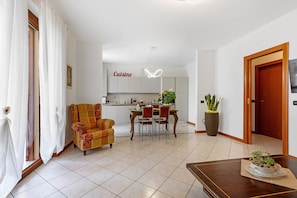 A living room with a sofa, dining table, and chairs, a kitchen area with cabinets and a countertop, and a large potted plant.
